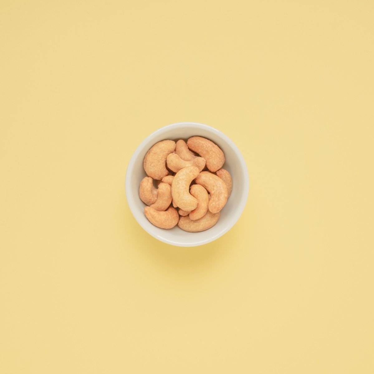 Cashew nuts in white cup on yellow background and copy space